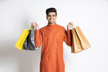 Happy young indian man holding shopping bags. male shopper wearing ethnic outfit,isolated over...