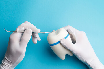 The concept of dental health and dental care. Dentist's day. Hands in white gloves hold a diagnostic probe and treat a white tooth on a blue background. Space for copying. Close-up.