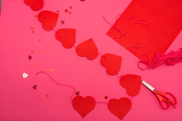 Diy hearts made of felt.red pieces of felt, carved in the shape of a heart. Scissors, thread, buttons, needle on a red background. A gift for Valentine's Day, wedding, mother's Day.