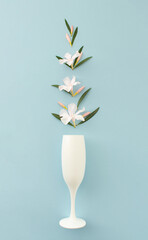 Artistic arrangement made of white tropic flowers and champagne glass on blue background. Minimal summer party or celebration concept.