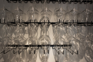 Wine glasses suspended on shelves against a light wall background.
