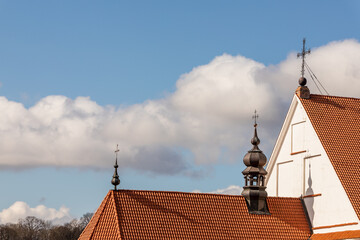 Fototapeta na wymiar Three metal crosses at the red stone rooftops against light blue and white gry cloudy sky at early spring. Detail of the church roof with crosses. Catholic cathedral rooftop with crosses at Kaunas.