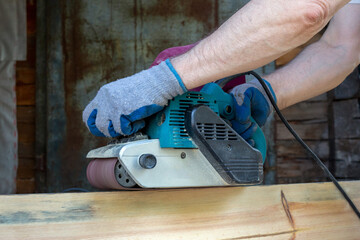 A man grinds wooden boards with a grinder. Woodwork, carpentry, hobby.