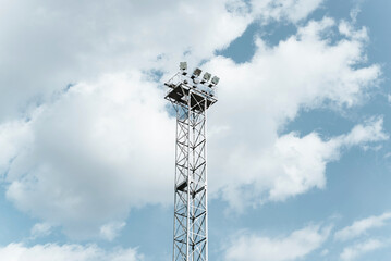 High lighting tower with spotlights against cloudy blue sky outdoors