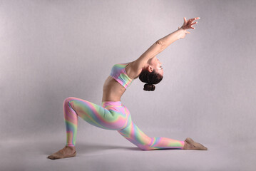 A beautiful slender gymnast in a stretch in a tracksuit does sports or yoga in the studio