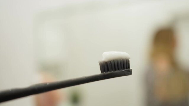 female hands hold a black toothbrush and squeeze white toothpaste onto it