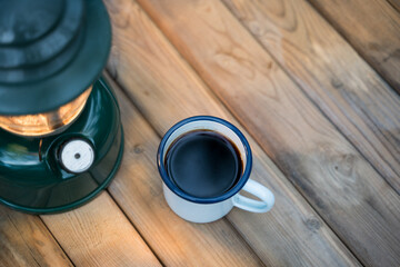 Selective focus white enamel coffee mug and coffee set in the garden with ancient lanterns in a camping atmosphere.
