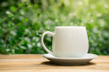 white ceramic coffee mug On the wooden floor, green tree bokeh background.