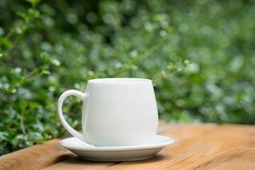 white ceramic coffee mug On the wooden floor, green tree bokeh background.