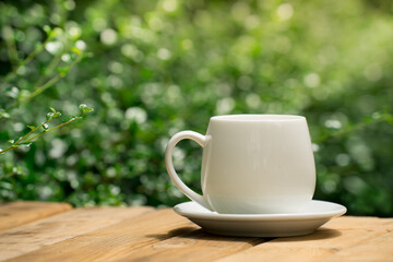 white ceramic coffee mug On the wooden floor, green tree bokeh background.