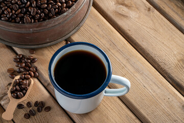 white enamel coffee mug and Dark Coffee beans on the old wooden floor. 