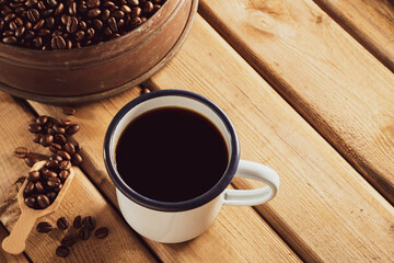 white enamel coffee mug and Dark Coffee beans on the old wooden floor.