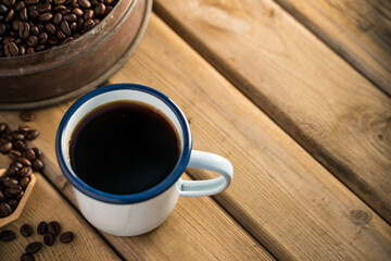 white enamel coffee mug and Dark Coffee beans on the old wooden floor.