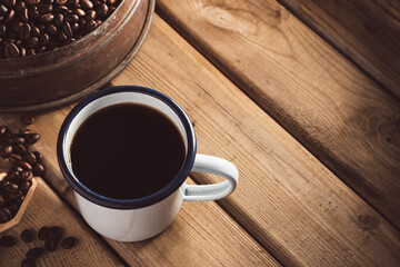 white enamel coffee mug and Dark Coffee beans on the old wooden floor.