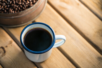 white enamel coffee mug and Dark Coffee beans on the old wooden floor.