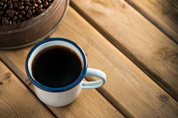 white enamel coffee mug and Dark Coffee beans on the old wooden floor.