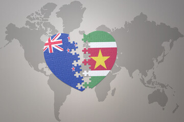 puzzle heart with the national flag of new zealand and suriname on a world map background. Concept.