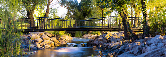 Panorama in the park at sunset, a small bridge over the stream, stone banks. Long shutter speed