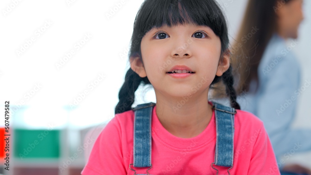 Wall mural Portrait of cute kindergarten girl with plait on hair speaking and talking in classroom learning and playing with friends spending school day with happiness, Happy learning concept