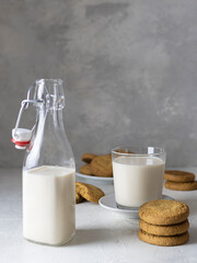 Oatmeal cookies and a glass of fresh milk on a light table. A bottle of milk in the foreground. Light gray background, text space