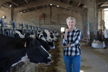 Adult female is standing at her workplace near cows at the farm.