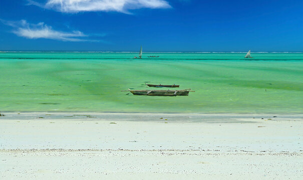 Beautiful empty deserted bright white sand beach, turquoise green shallow calm sea, traditional wooden dau boat, clear blue sky horizon - Zanzibar, indian Ocean