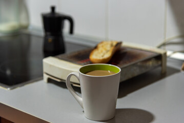 Cup of coffee with milk on the kitchen counter, with a toaster and a coffee pot in the background.
