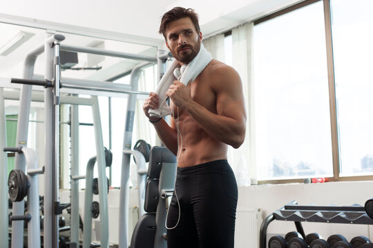 Young fit man in gym, fitness, listening to music, with towel, lifting weights