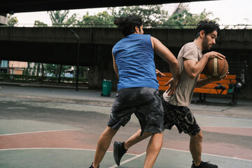 Two caucasian men pratice baskegball in court at urban street.