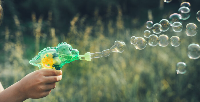 Dinosaur soap bubble gun shooter, blower. Party for kids. Girls,chidren playing funny family game with dad, father. Outdoors activity in summer in green park. Big flying bubbles