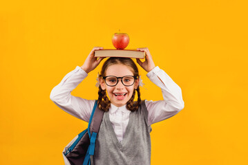 Back to school kid. Happy child holds a book and a red Apple in her head on a yellow background....