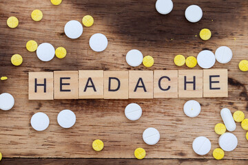 wooden block with the word headache written on it with a wooden backdrop and medicine