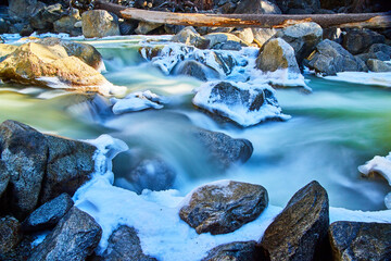 Early spring detail of river cascading falls over rocks covered in snow and frost