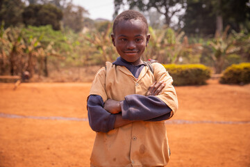 portrait of a young African child with Down syndrome, he has his arms crossed and looks at the...