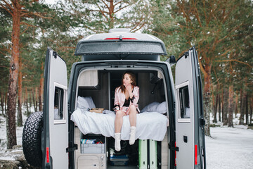 Young woman inside her campervan in winter relaxing and looking outdoors