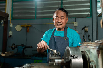 A senior craftsman who is skilled in craftsmanship, is controlling, skillfully operating a lathe, is in a small factory that is his family business. - obrazy, fototapety, plakaty