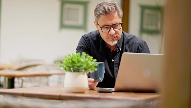 Casual middle age man sitting in garden working on laptop computer in home office. Businessman tele working