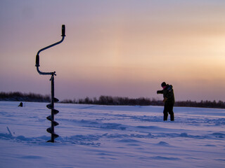 Ice drill on a frozen lake with a fisherman in the background.