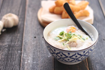 Congee in a Thai-patterned cup and fried batter served in an Asian-style cup on a black table with fried batter that we call 