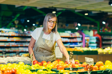 Senior female store worker lays out and sorts fruit in the fruit department