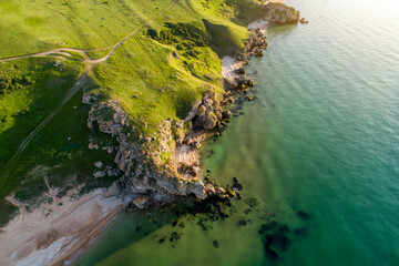 Aerial view of beach. Big hills around. Sunny day at dawn. Greenish sea. Drone Photo.