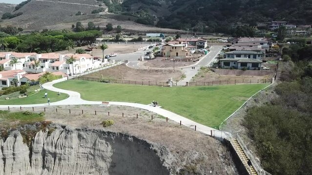 aerial footage of the vast rippling blue ocean water with majestic mountain ranges and beach front homes along the coastline with lush green grass and trees and blue sky at Pismo Beach in California