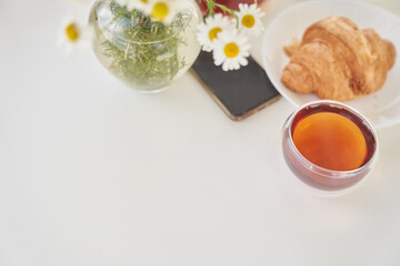 Top view of fresh sweet croissants on the table with tea and a vase of daisies. In the middle of the table is a smartphone with a place to copy. High quality photo
