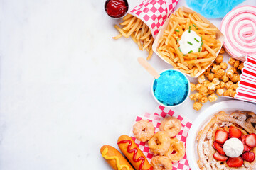 Carnival theme food side border on a white marble background. Above view with copy space. Summer fair concept. Corn dogs, funnel cake and snacks.