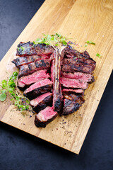 Modern style traditional barbecue dry aged wagyu porterhouse beef steak bistecca alla Fiorentina with herbs and spice sliced and served as close-up on a wooden design board
