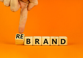 Time to rebrand symbol. Businessman turns wooden cubes and changes the concept word Brand to Rebrand. Beautiful orange table orange background. Business brand or rebrand concept. Copy space.