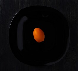 orange tomato placed in the center of a black plate