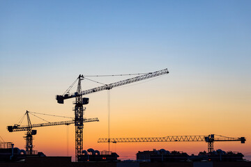 Silhouettes of tower cranes on construction site at sunset	