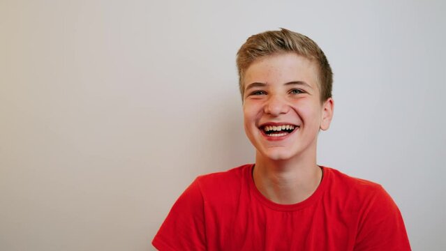 Happy positive teenage boy laughing at funny joke looking at camera on the wall background. Cheerful teen having fun, smiling face. Headshot close up portrait.