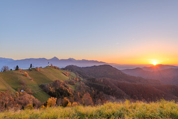 Church on the hill at sunrise. Beautiful scenery at Jamnik, Slovenia. Panoramic view of the mountains behind the church in the early morning.